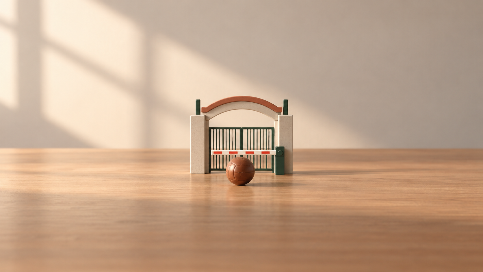A miniature entry gate with a barrier and an unmarked leather sports ball on a table.