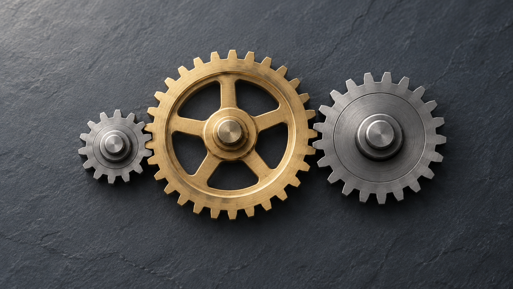 Conceptual illustration of a brass gear linked to two differently sized steel gears on slate.