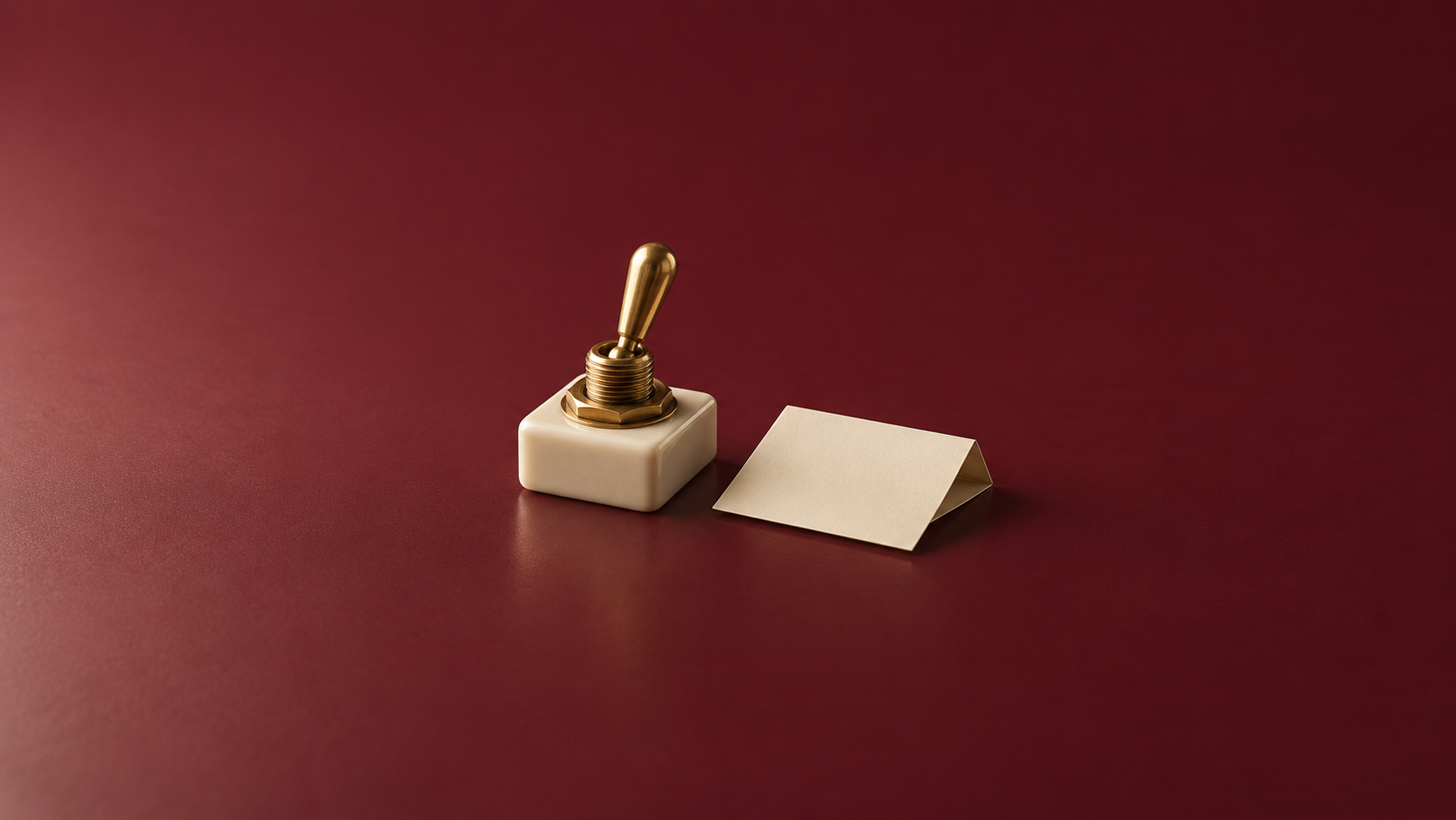 Un interruptor de palanca de latón sin marcas sobre una base cerámica marfil junto a una hoja doblada en una superficie burdeos.