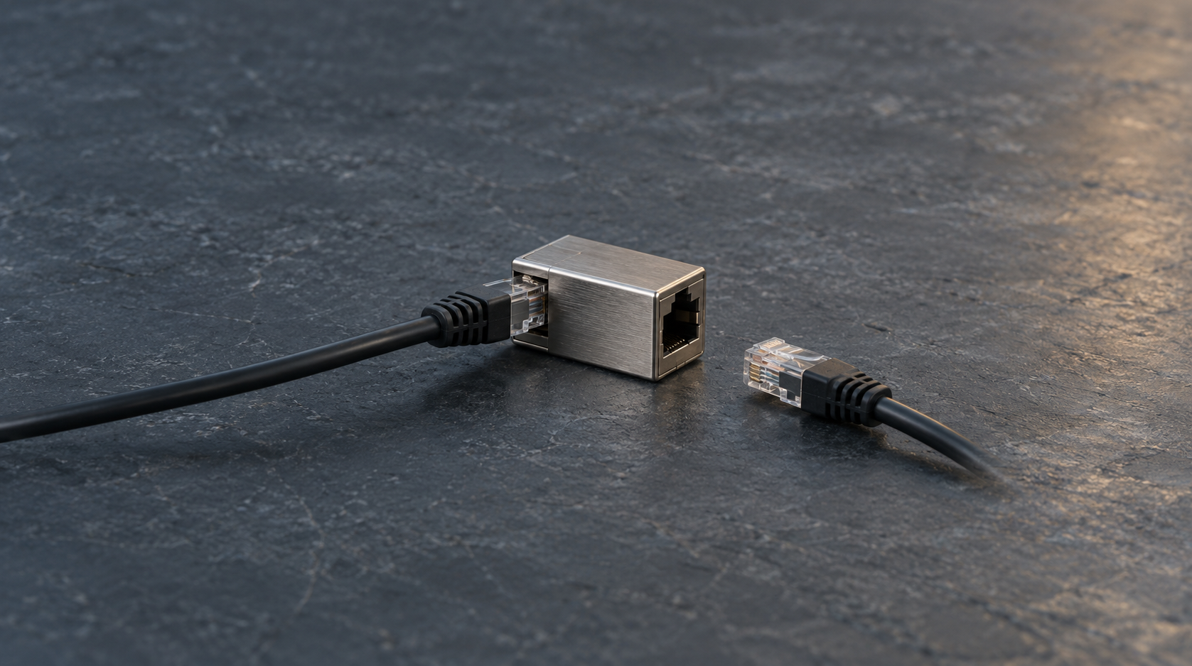 Un acoplador de red metálico con un cable conectado y un conector suelto sobre una mesa de pizarra.